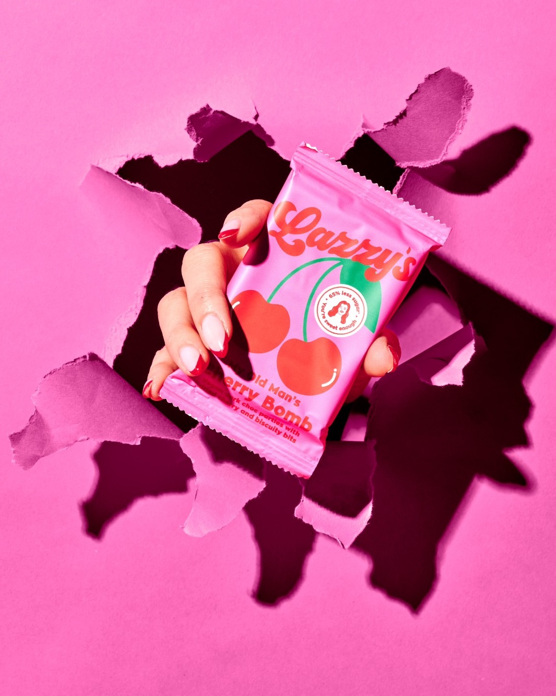 Hand bursting through pink paper holding a Cherry Bomb bar